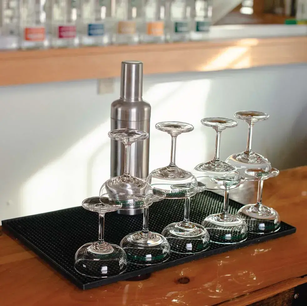 Upside-down wine glasses drying next to a metal shaker on a wooden counter.