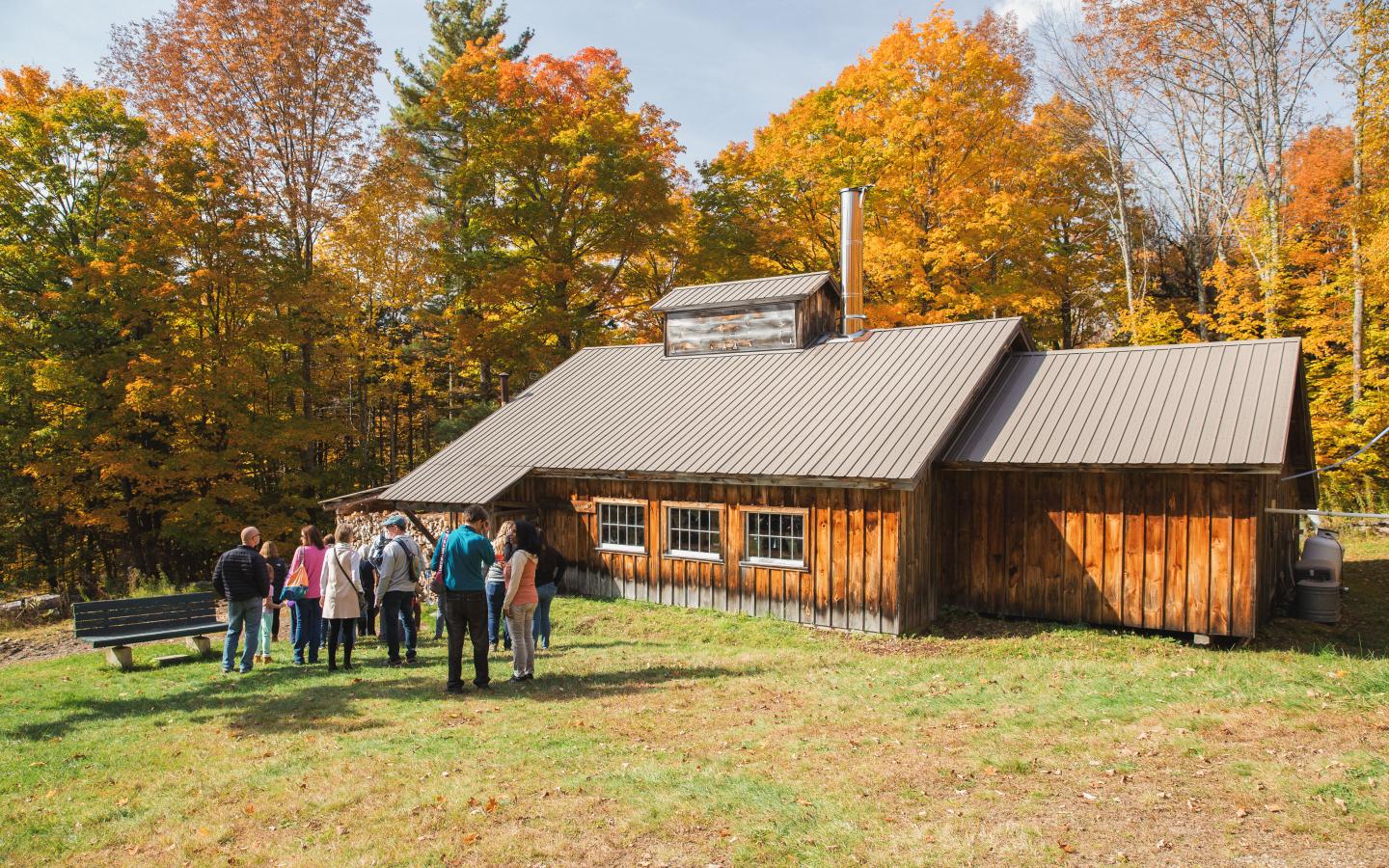A group of people near a wooden cabin with autumn trees.