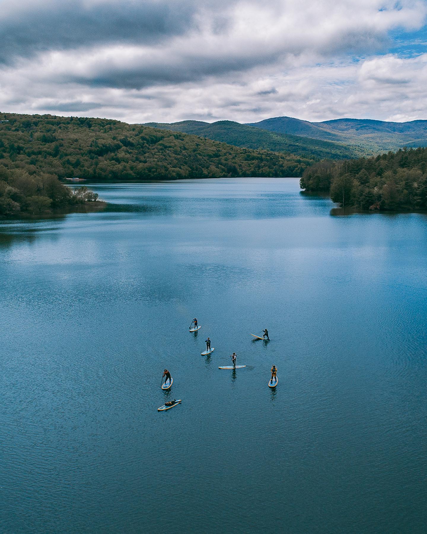 Paddleboarders on a calm lake surrounded by hills under a cloudy sky.