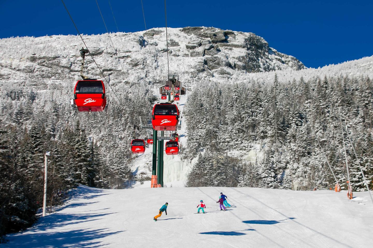 Red cable cars over skiers on a snowy mountain slope under a clear blue sky.