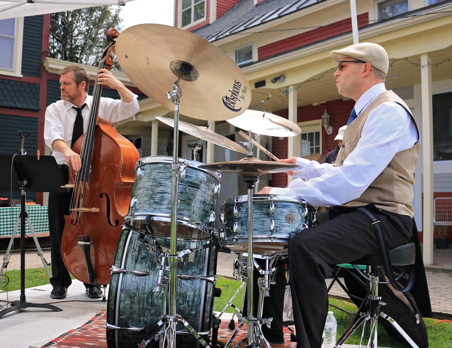 Drummer and double bassist performing outdoors near a house.