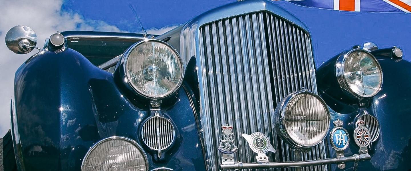 Blue vintage car front with chrome grille and headlights. British flag in the background.