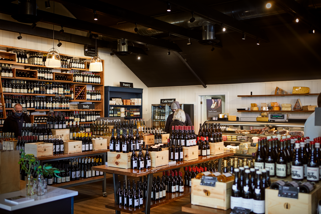 Wine shop with bottles on shelves and tables, warm lighting and wood accents.