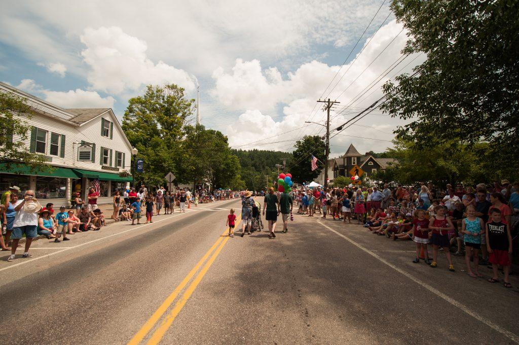 Street parade with spectators on both sides under a cloudy sky.