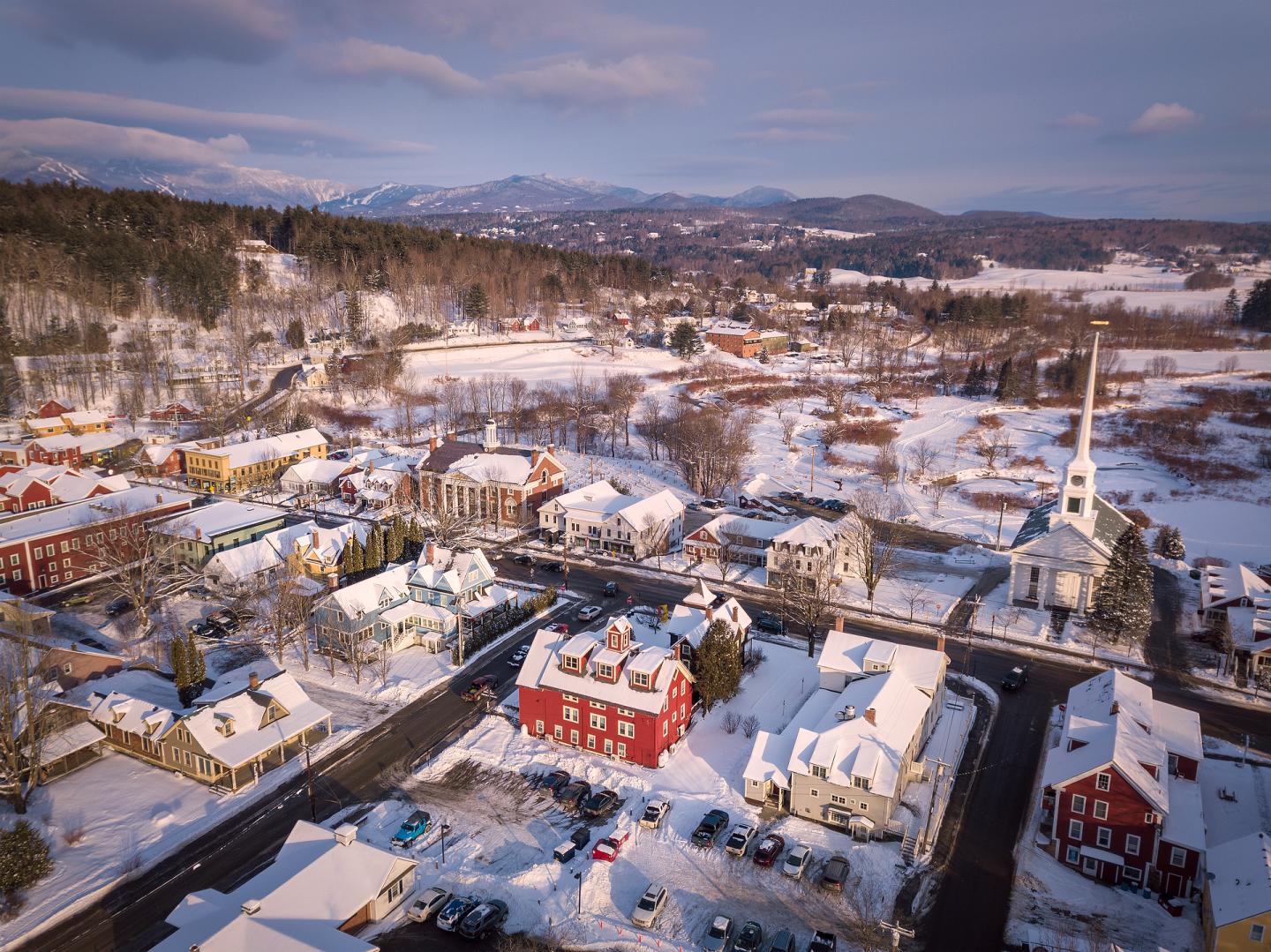 Snowy village with colorful buildings and a church steeple, mountains in the background.