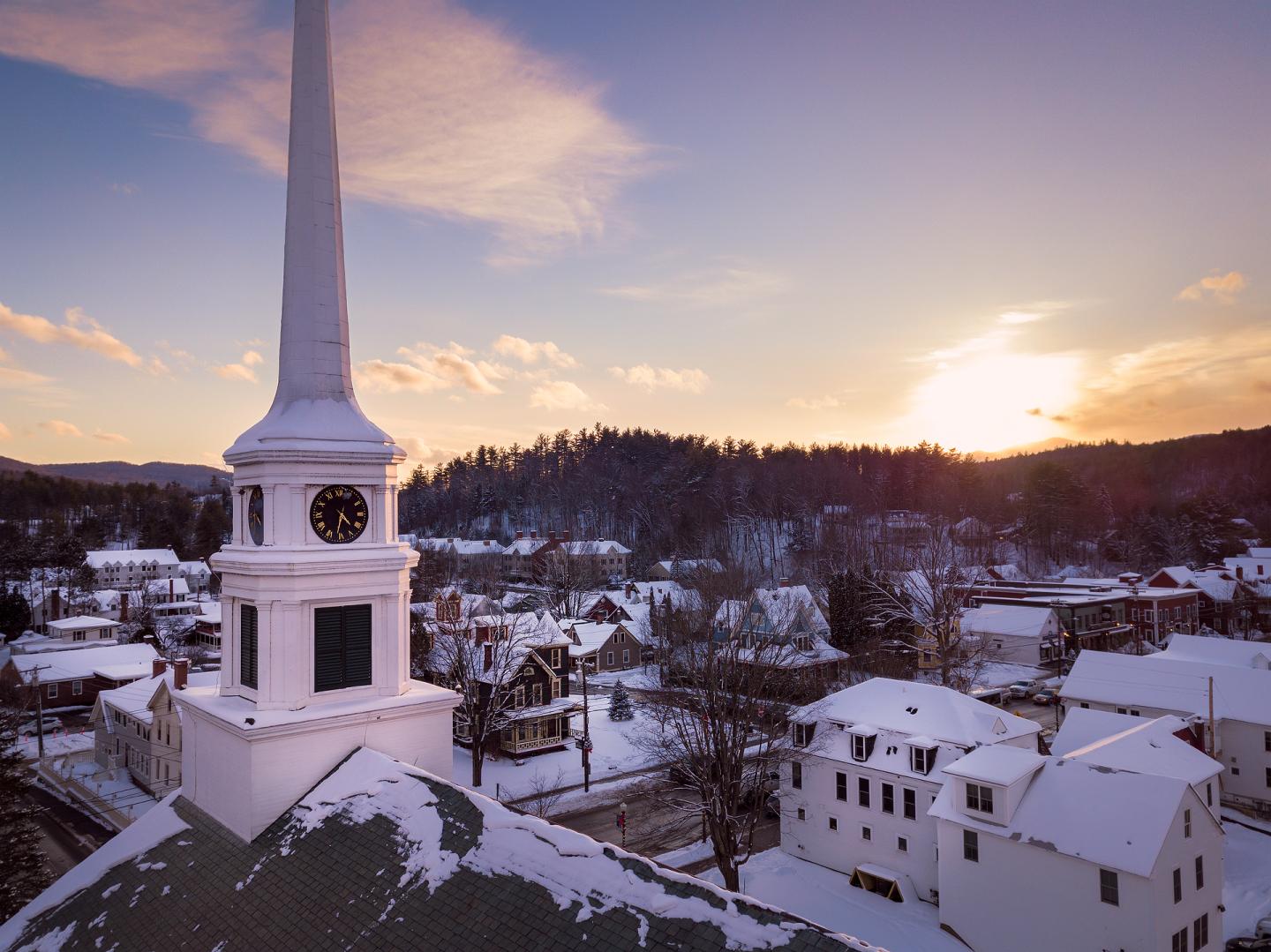 Church steeple with clock, snowy village at sunset.